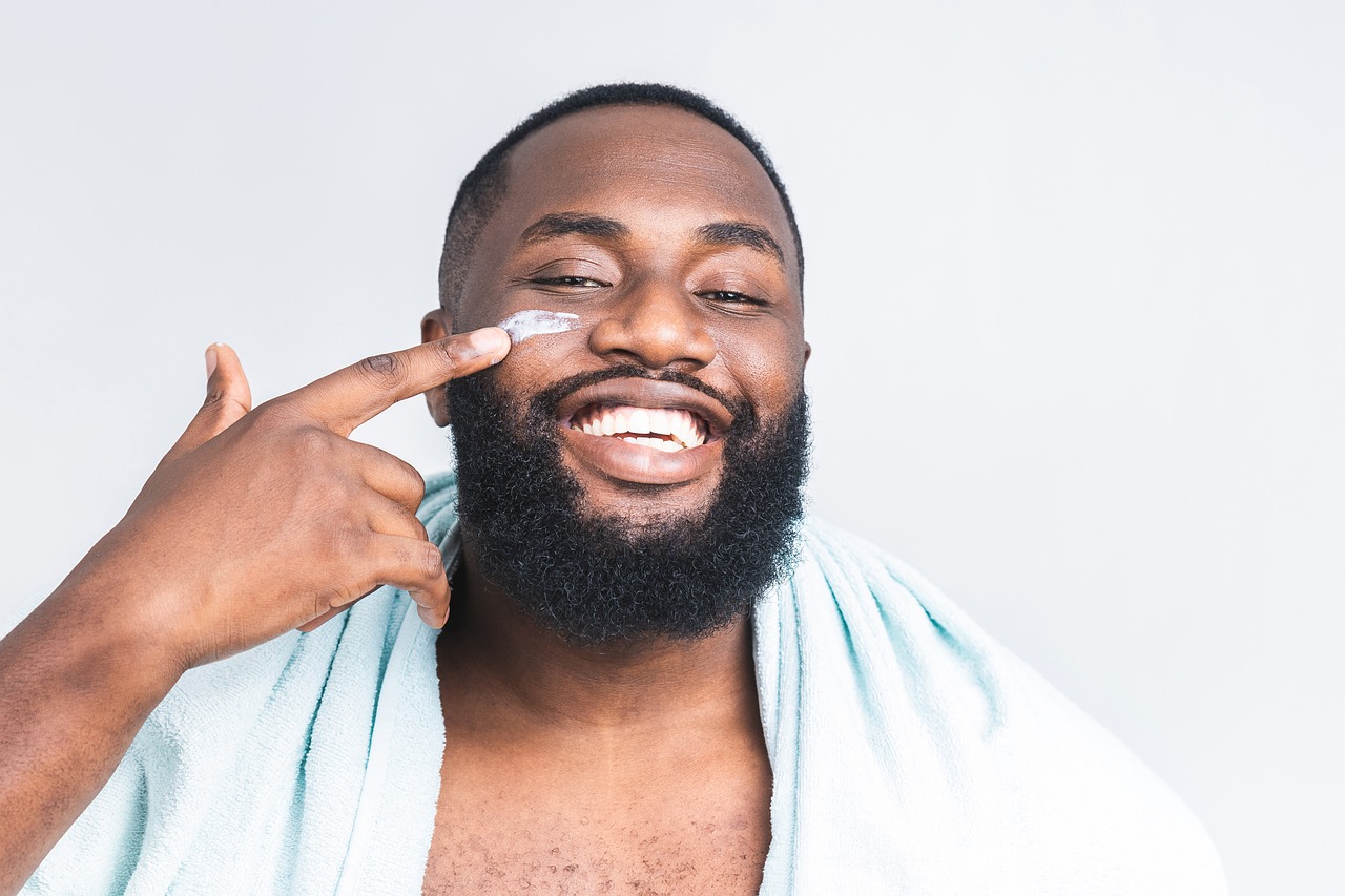 Smiling man applies face cream to his cheek.