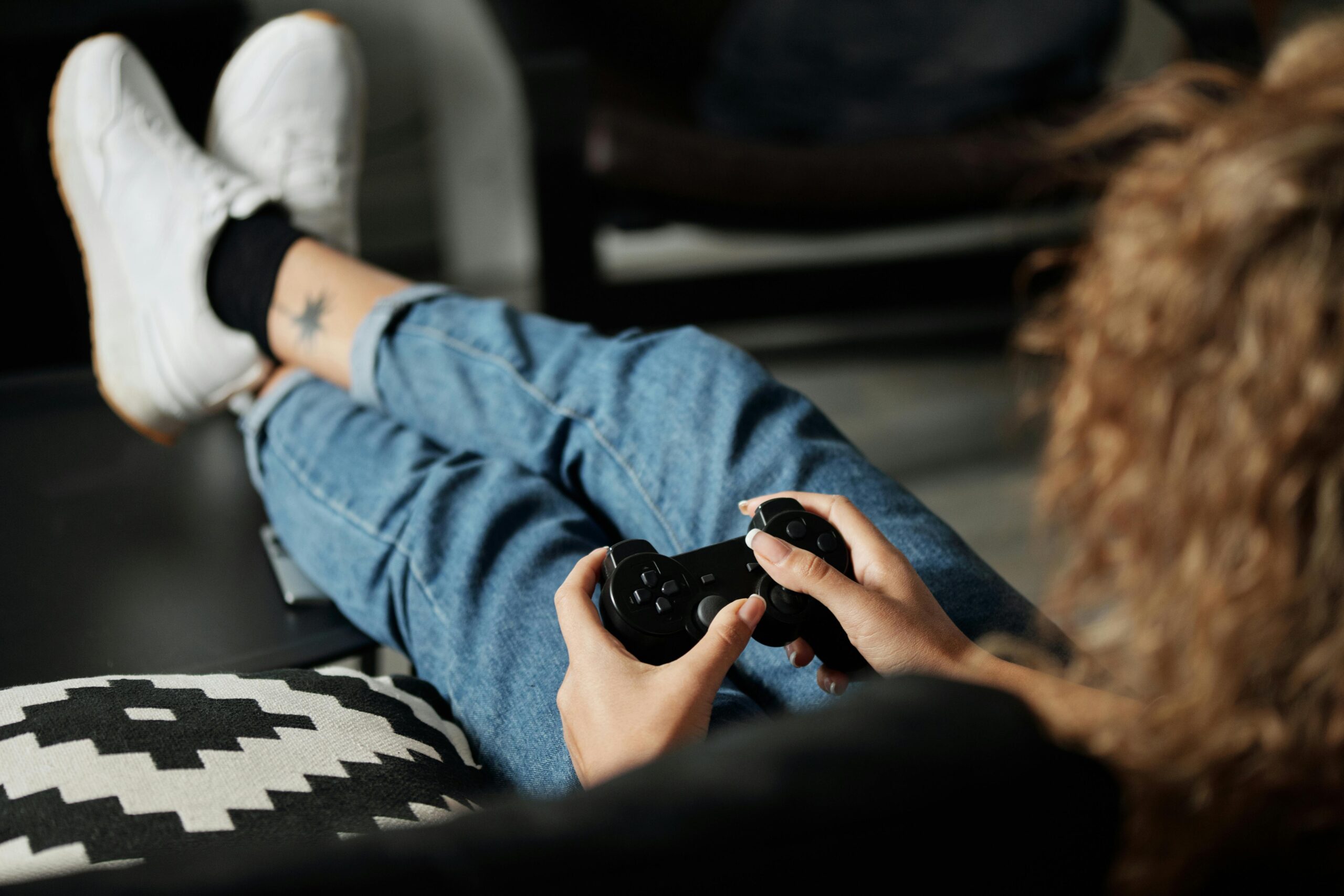 a woman sits on a sofa with her legs up looking cosy gaming on a PlayStation controller 