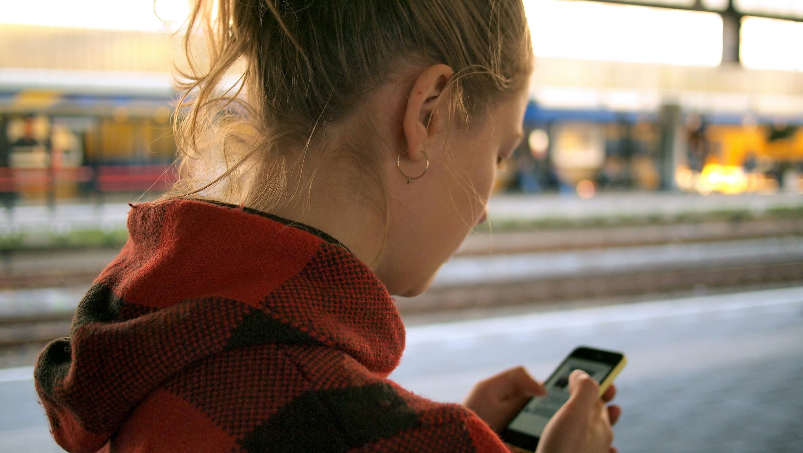 woman doomscrolls on her phone at train station