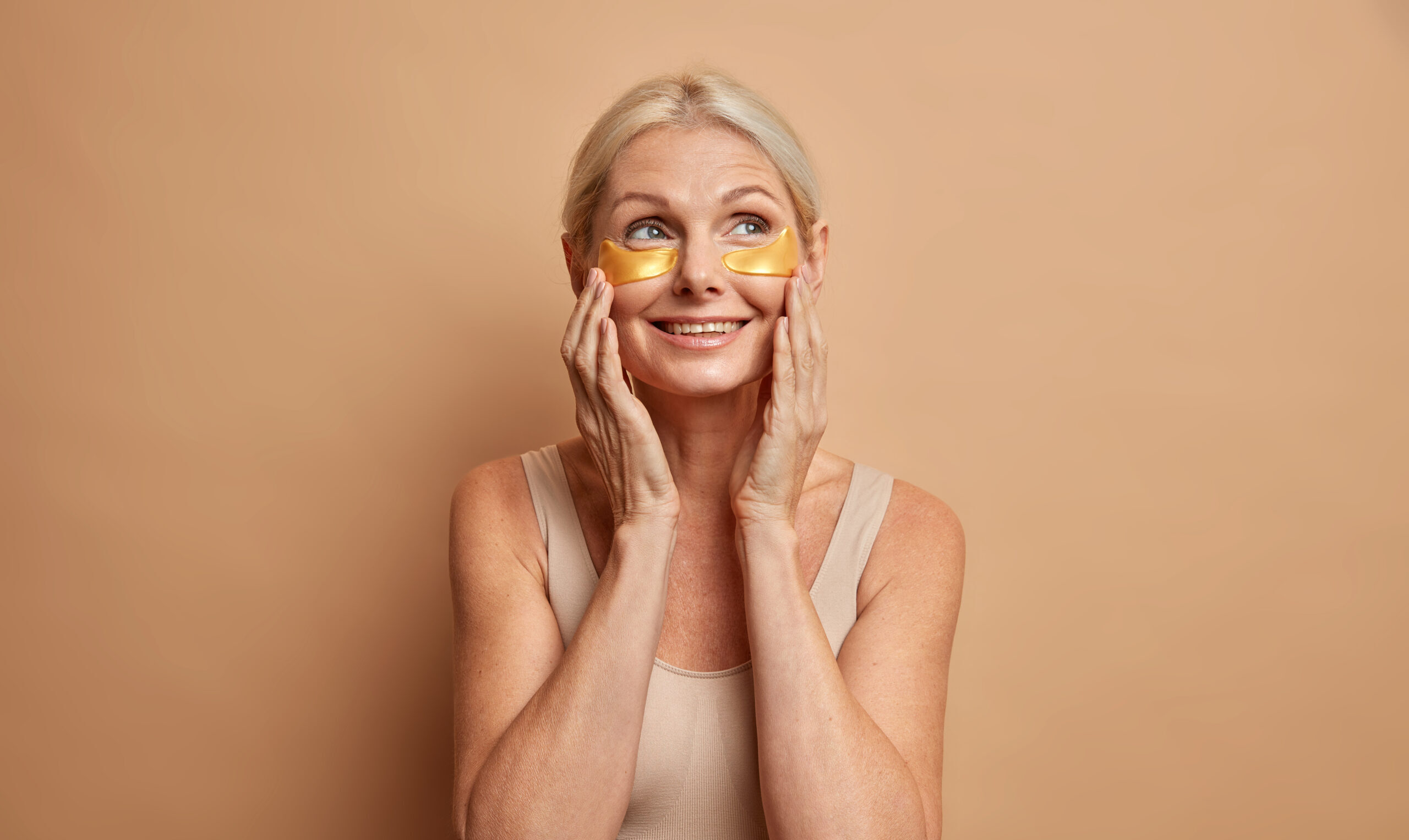 older woman wears gold undereye masks with brown backround 