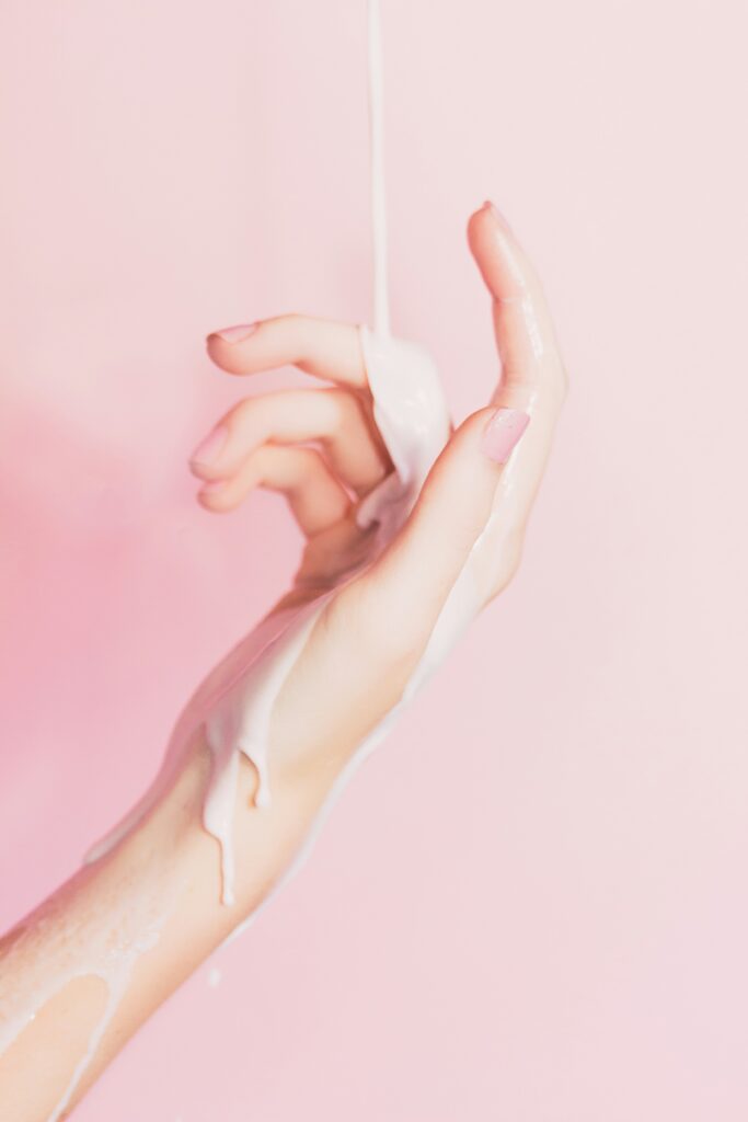 milky skincare pours down onto a hand in front of a pink background