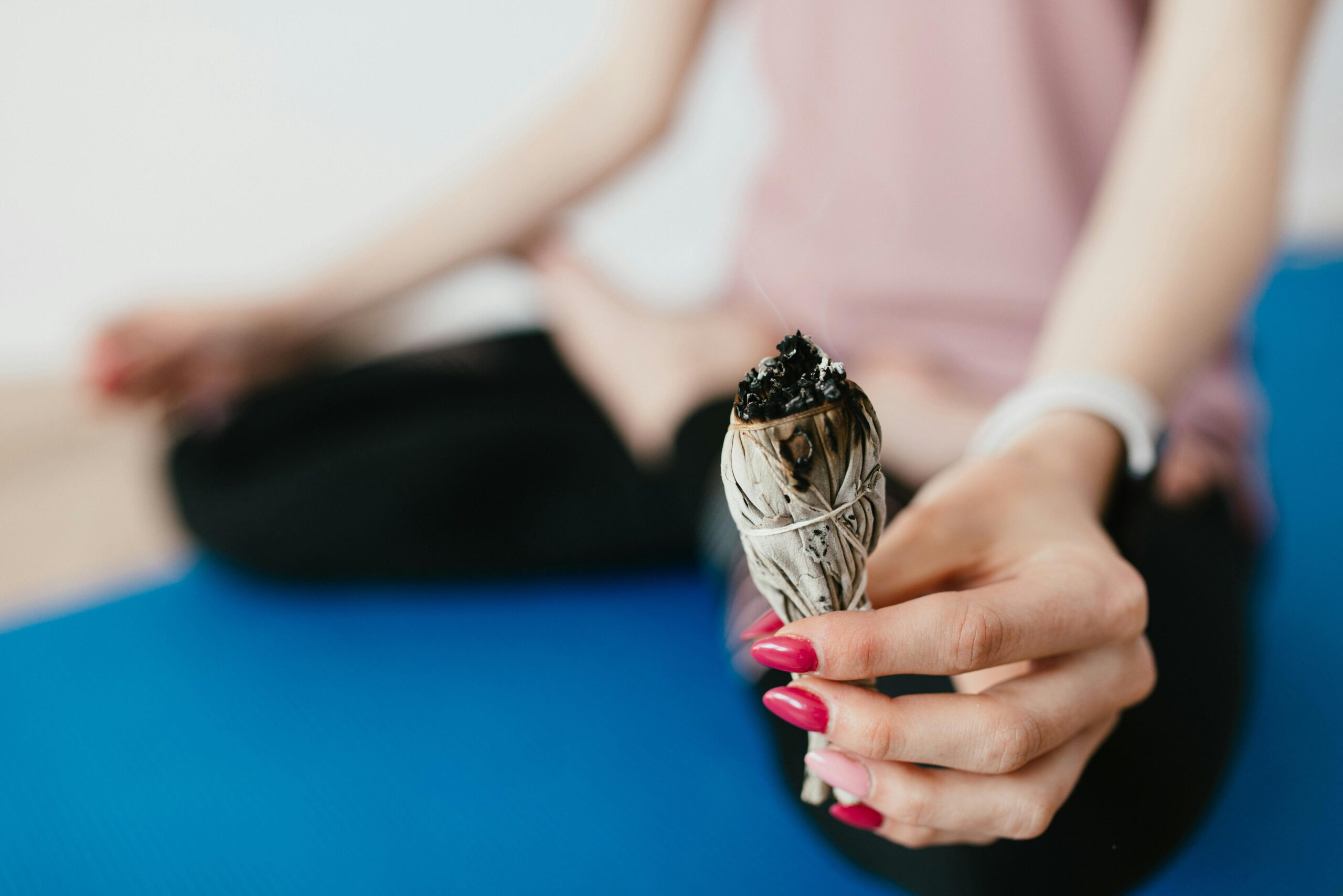 A woman sits meditating with burning sage to smudge her environment 