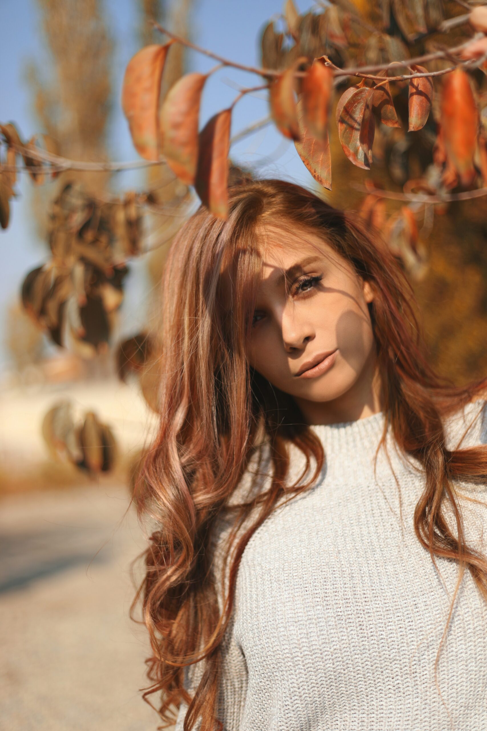 Woman with auburn hair poses by autumnal leaves