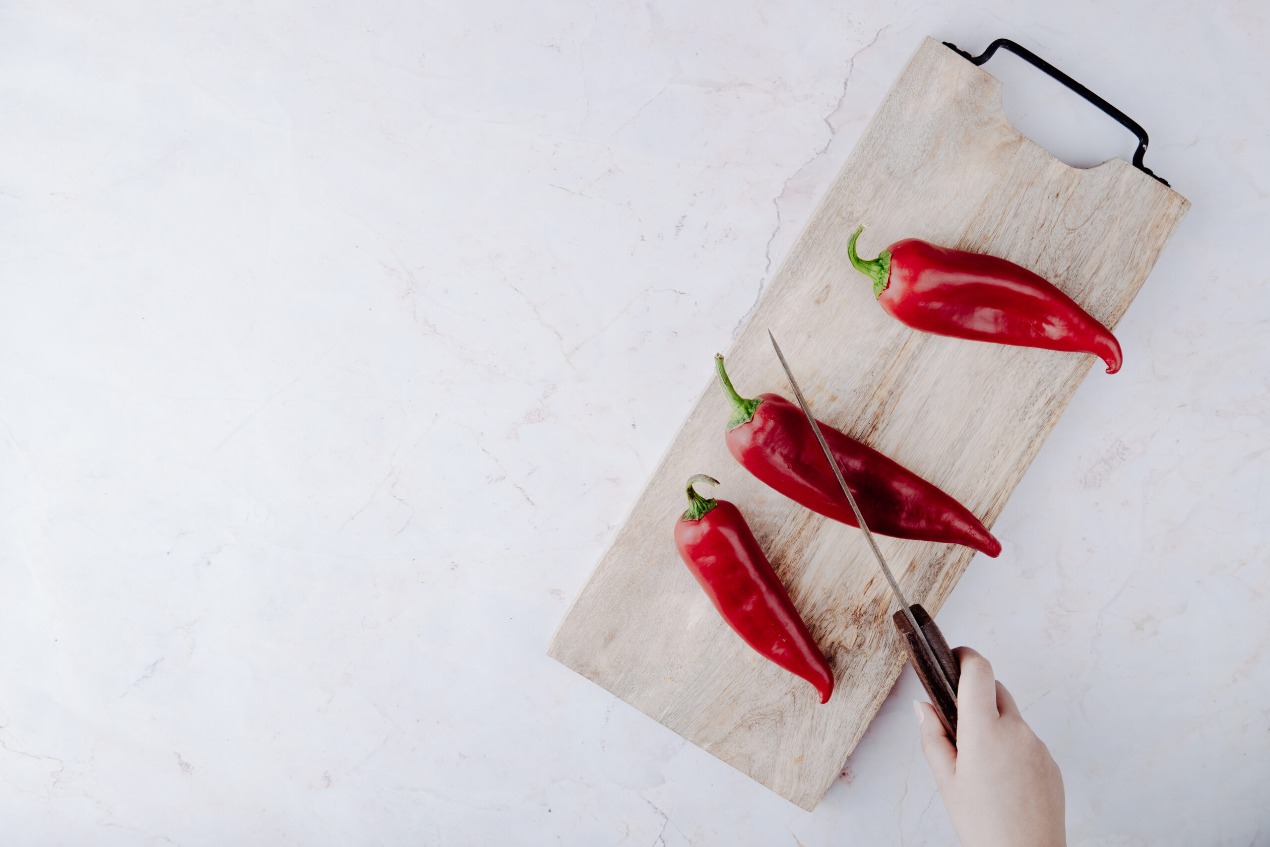 three red chillis on a chopping board with a knife about o cut through one