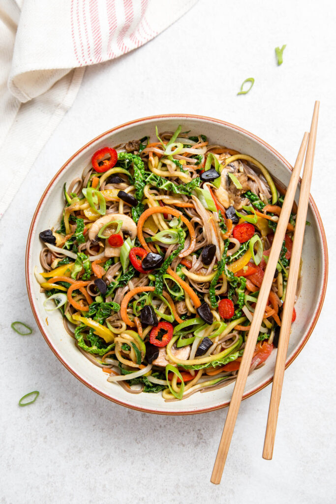 A bowl of Lo Mein made with black garlic and chopsticks on the side