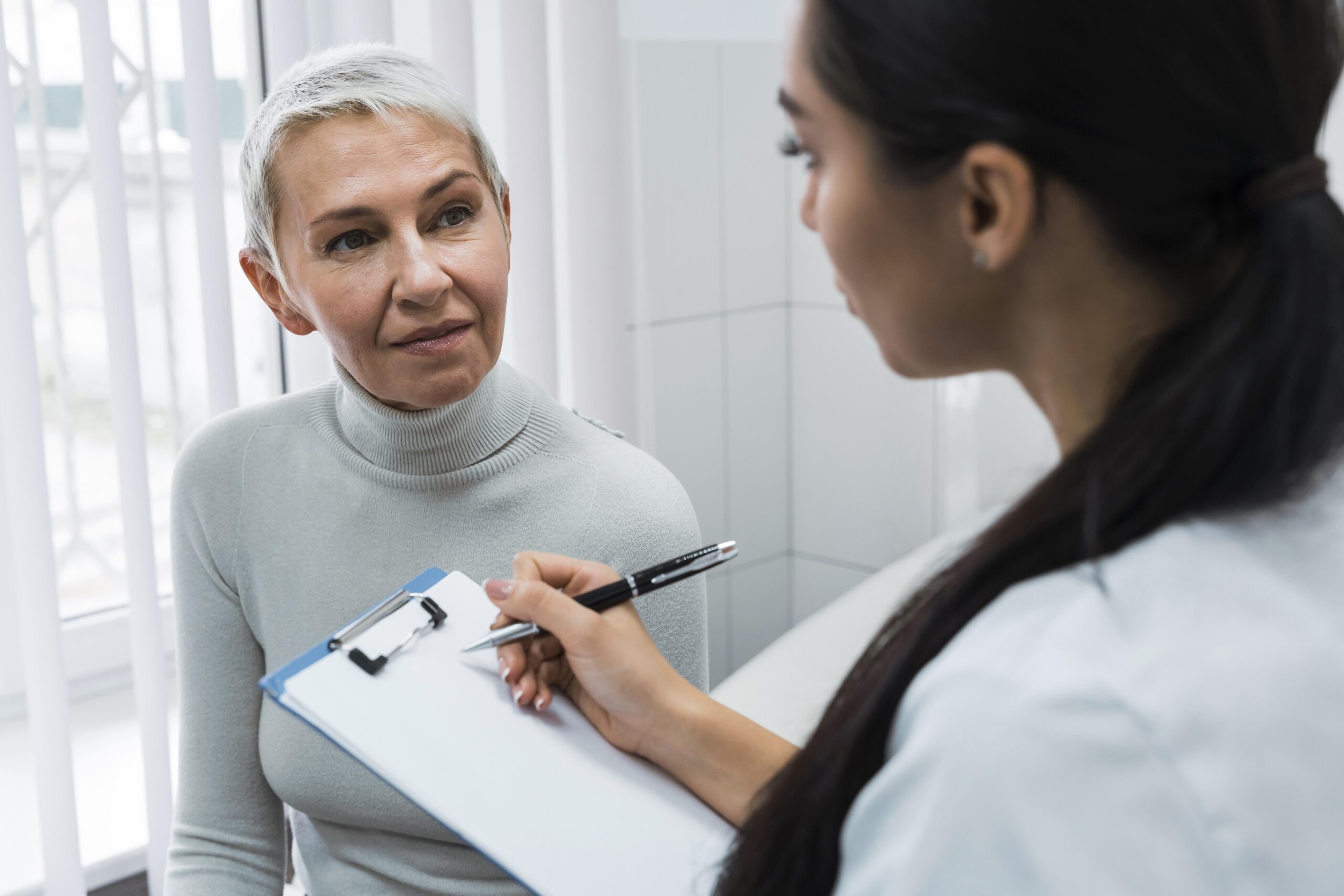 An older woman looks at a doctor who is taking notes