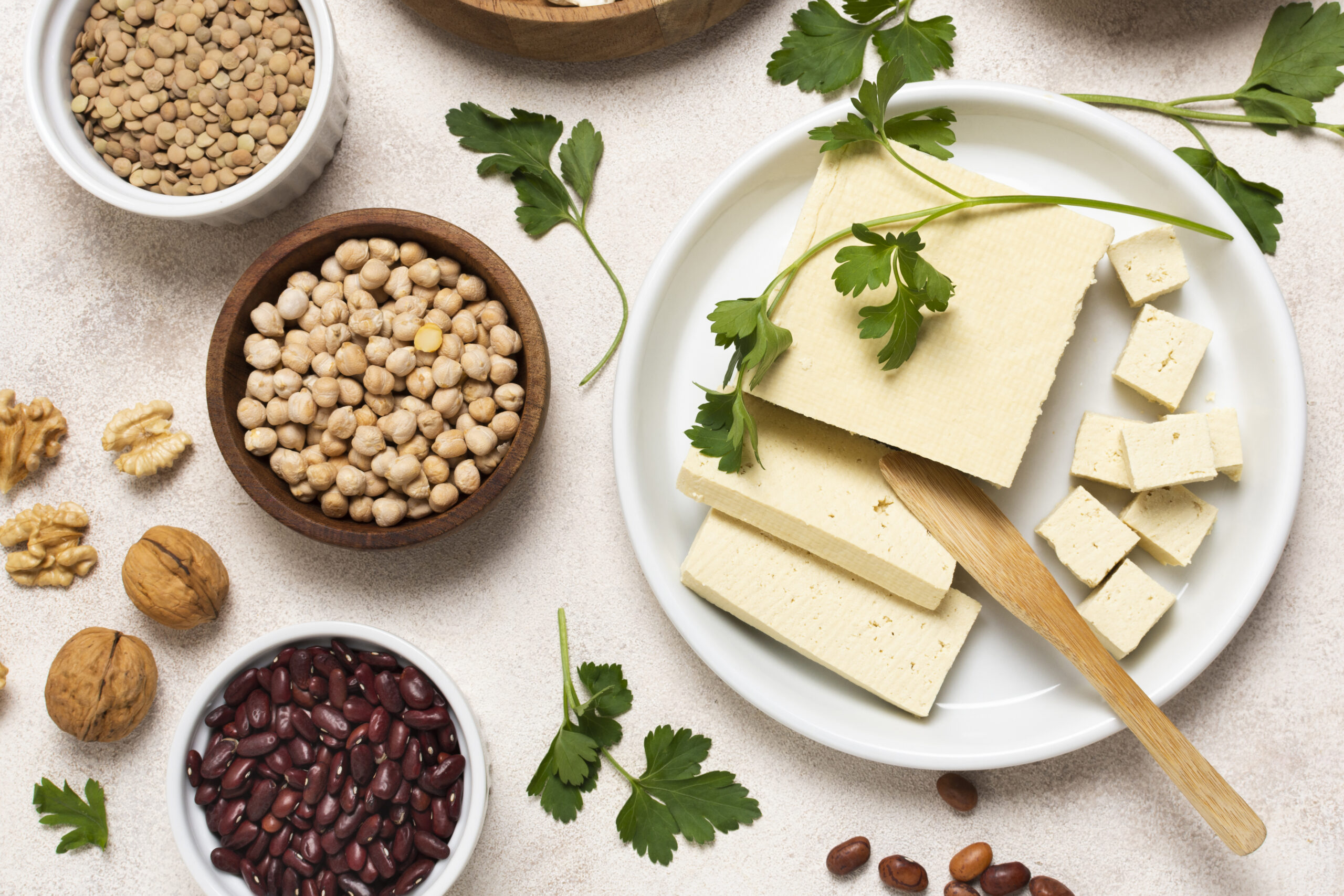 Different food laid out on a white table including tofu, walnuts, kidney beans and chickpeas 