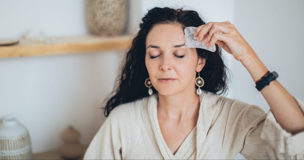 A woman uses a gua sha tool to tone her face.