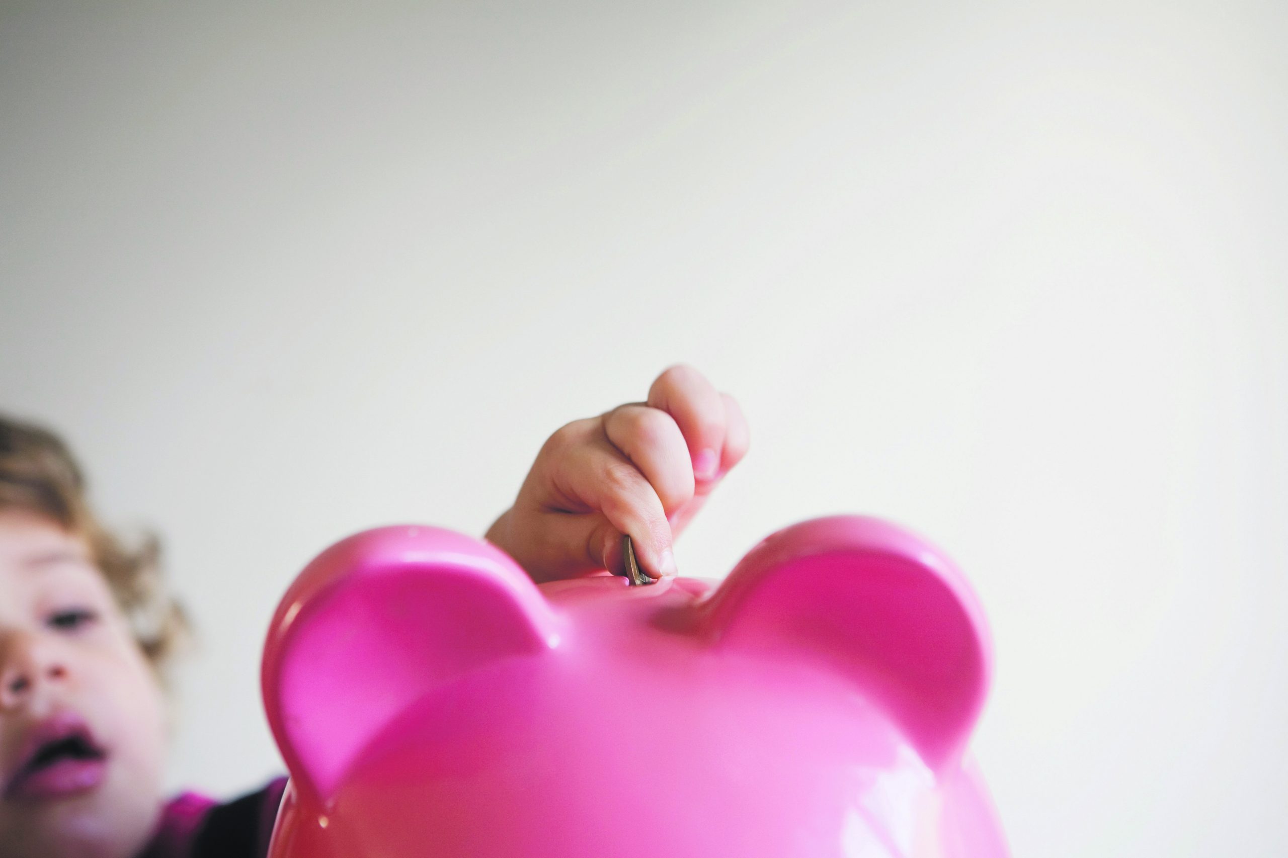 A kids saves some coins a in a pink piggy bank.