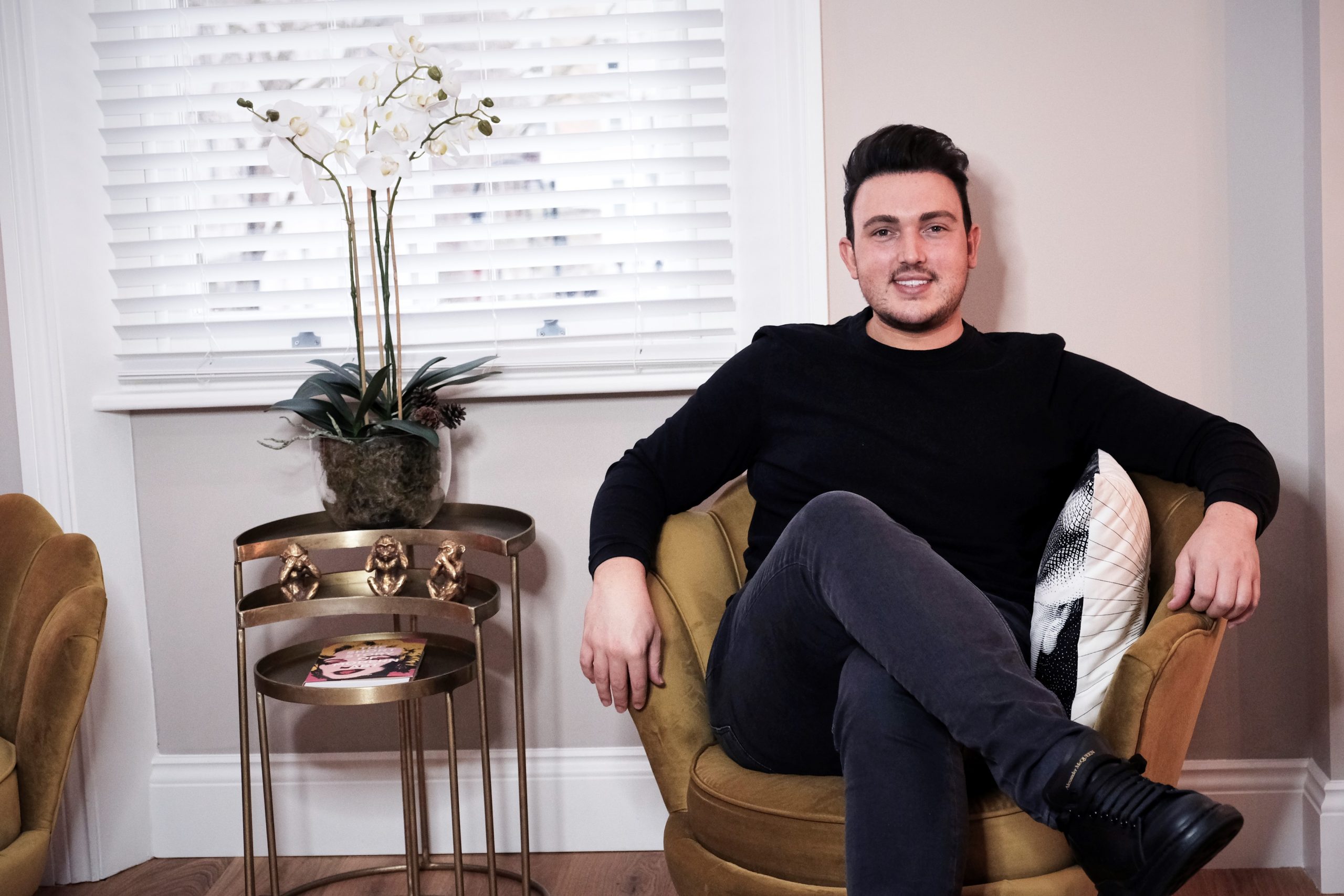 Skincare expert Shane Cooper sits with his legs crossed in an armchair