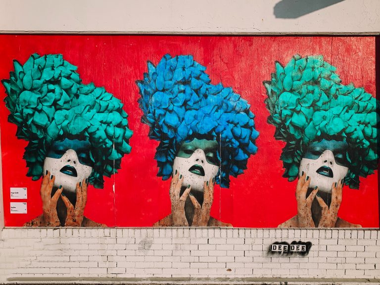 Mural of three women's faces with bouffont hair against a red backdrop