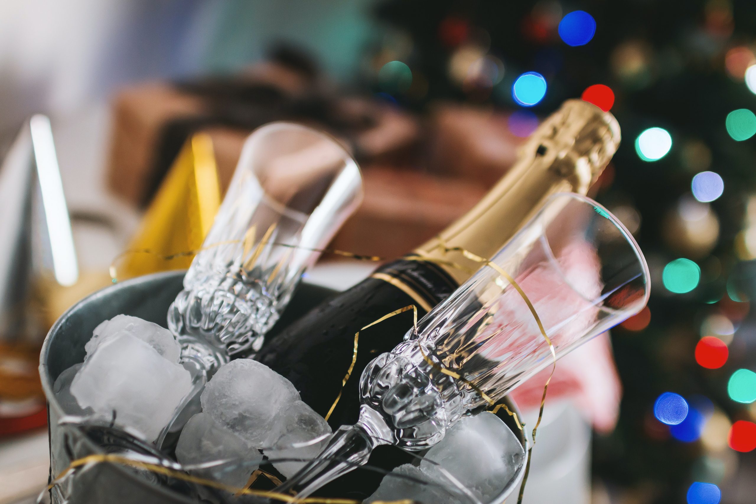 Champagne on ice with two crystal glasses against a blurred Christmas tree backdrop