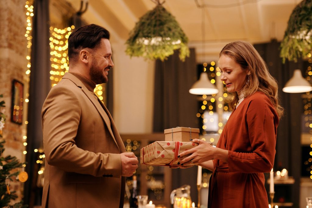 A woman in red gives two wrapped Christmas presents to her friend