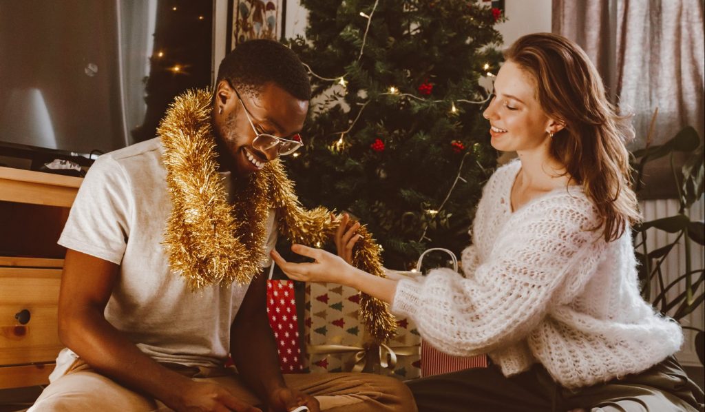 A young white woman adorns her black boyfriend with gold tinsel on Christmas