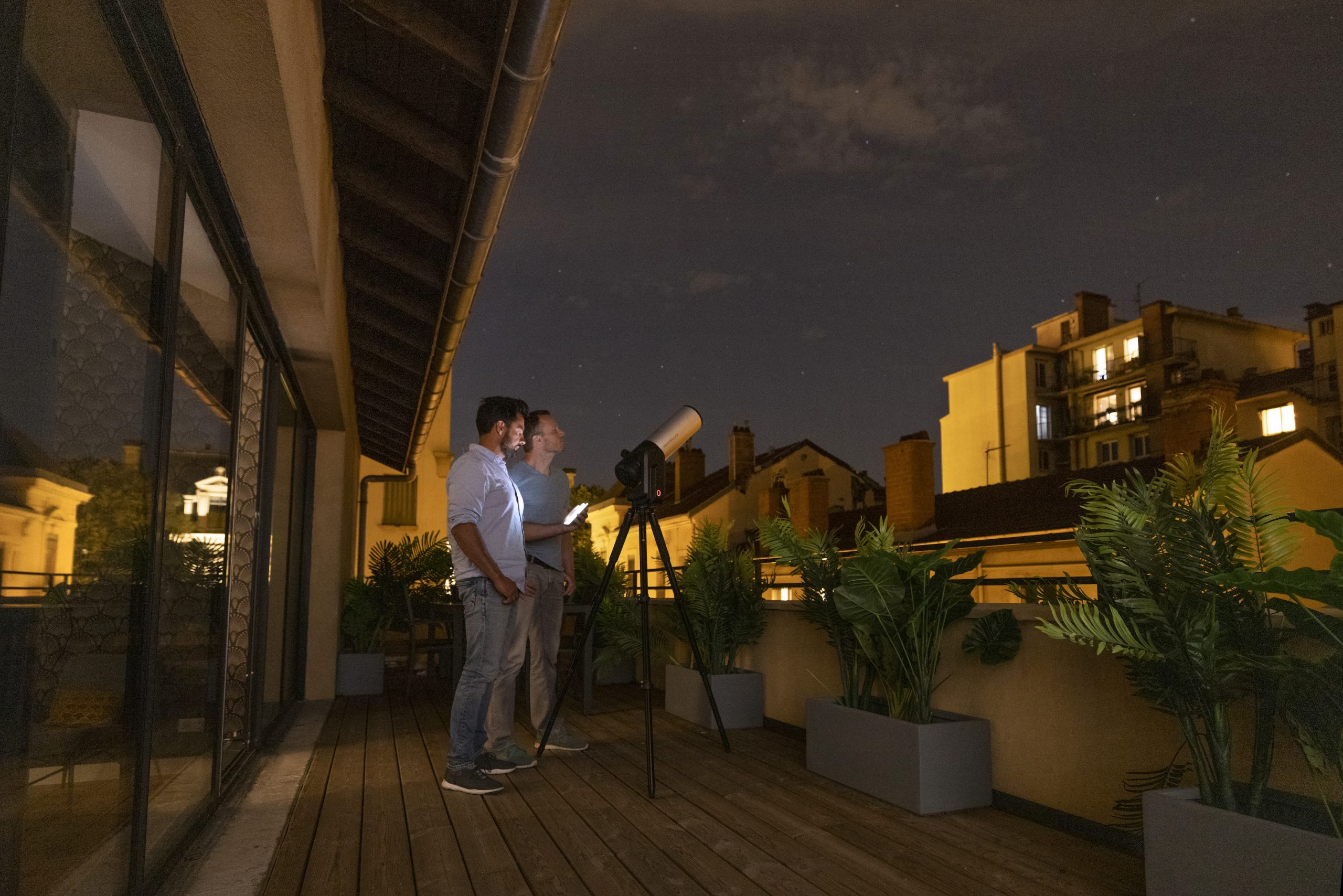 Two friends watch stars from their balcony with an Unistellar eVscope 2 telescope 