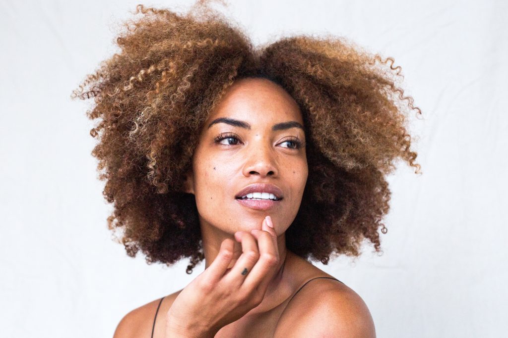 A beautiful black woman with a clear complexion and frizzy hair poses.