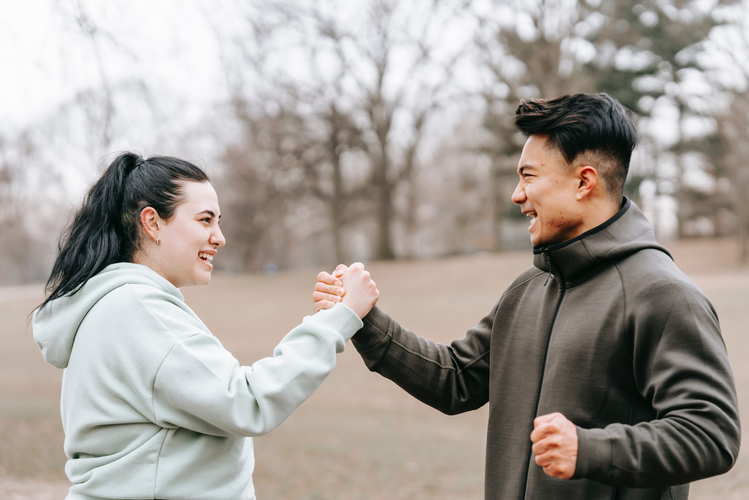 A man and woman in the park goad each other in their fitness goals with a power handshake.
