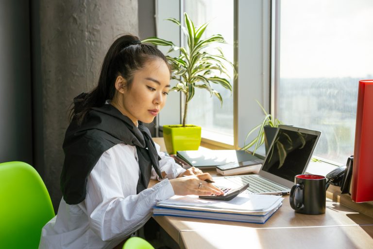 A young woman weighs up the pros and cons of savings accounts using a notepad and calculator.