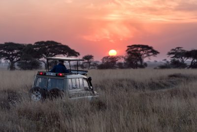 A jeep crosses the African savannah as the sun sets.