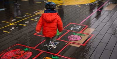A child in a red coat playing hopscotch at the Imagine Children's Festival