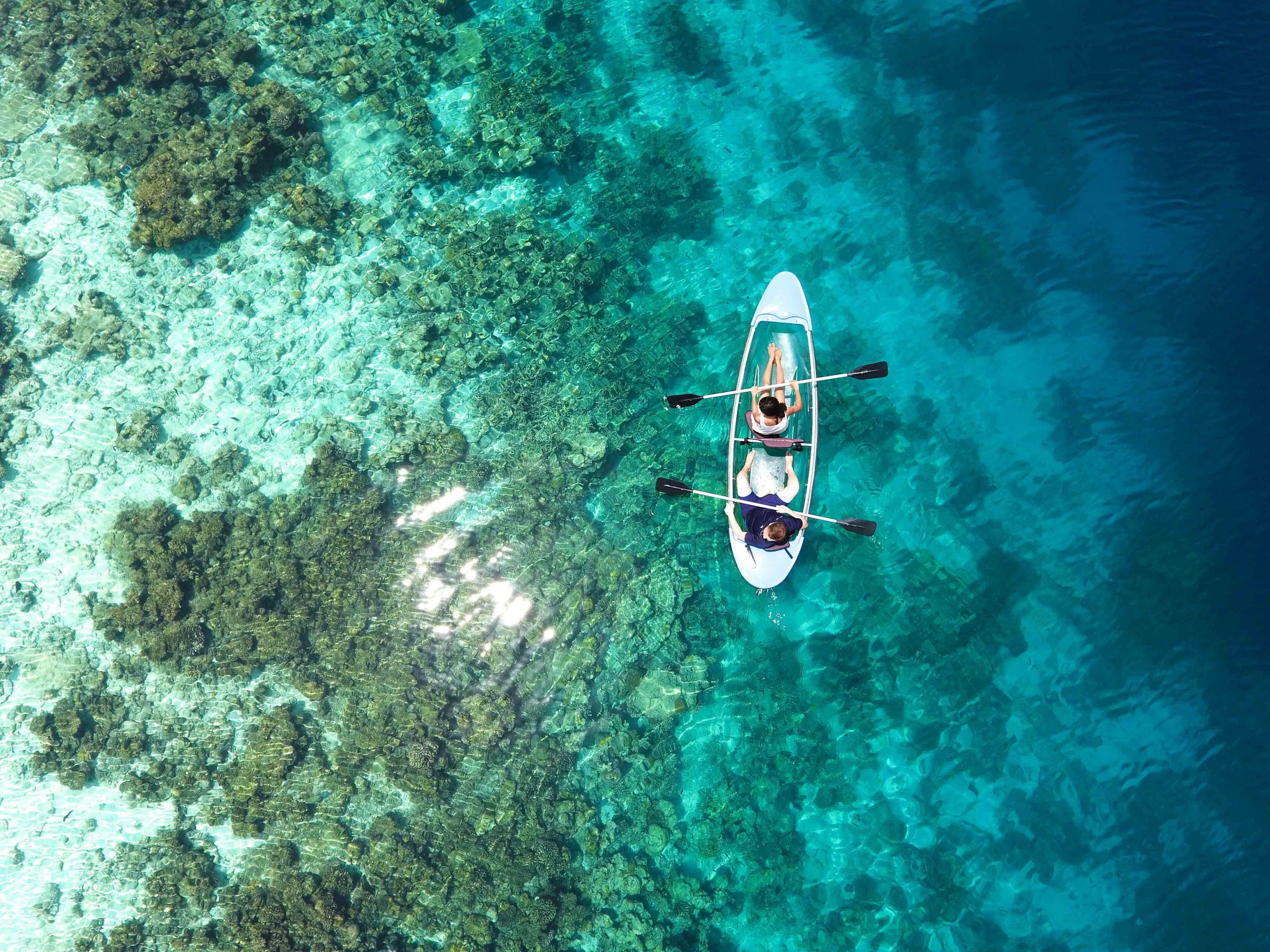 Aerial view of a canoe as it passes over a coral reef in the Maldives.