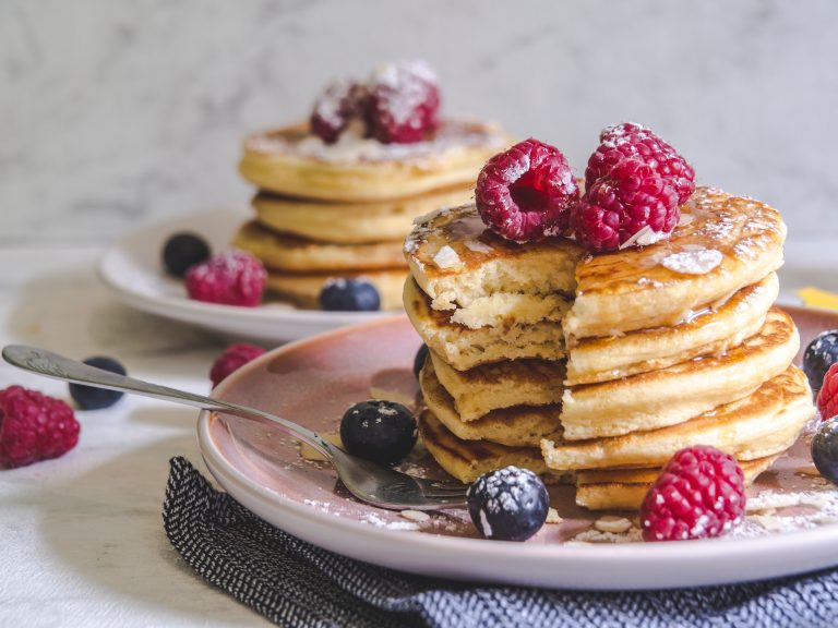 Two plates of pancakes served with raspberries and blueberries.