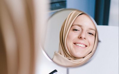 A woman smiles at her reflection in a hand mirror.