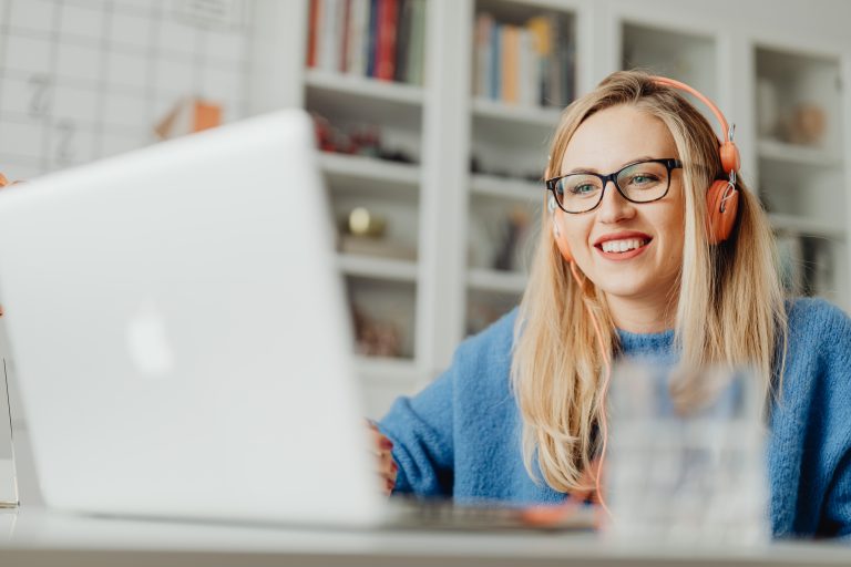 A young woman wearing glasses works with her colleagues virtually via her MacBook.