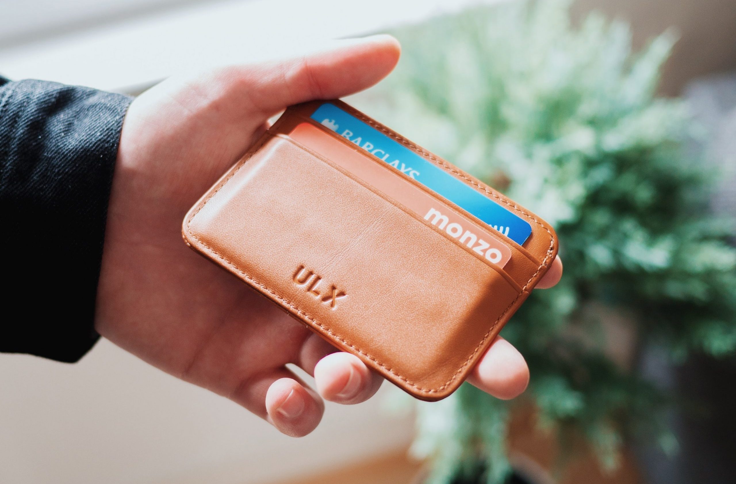 Close-up of a hand holding a leather wallet with two credit cards - monzo and Barclays.