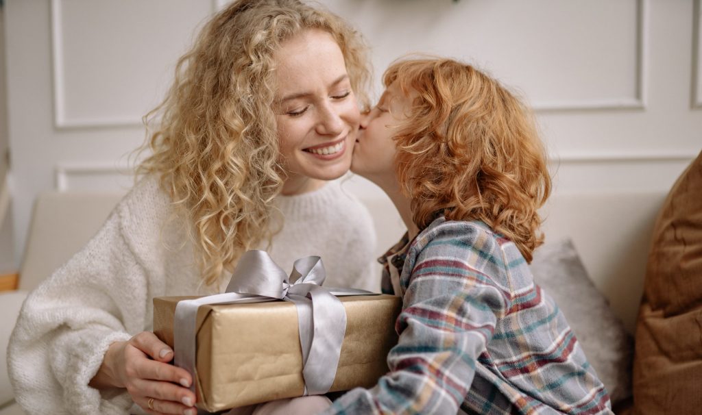 A young boy gives his mother a kiss and gift-wrapped present on Mother's Day.