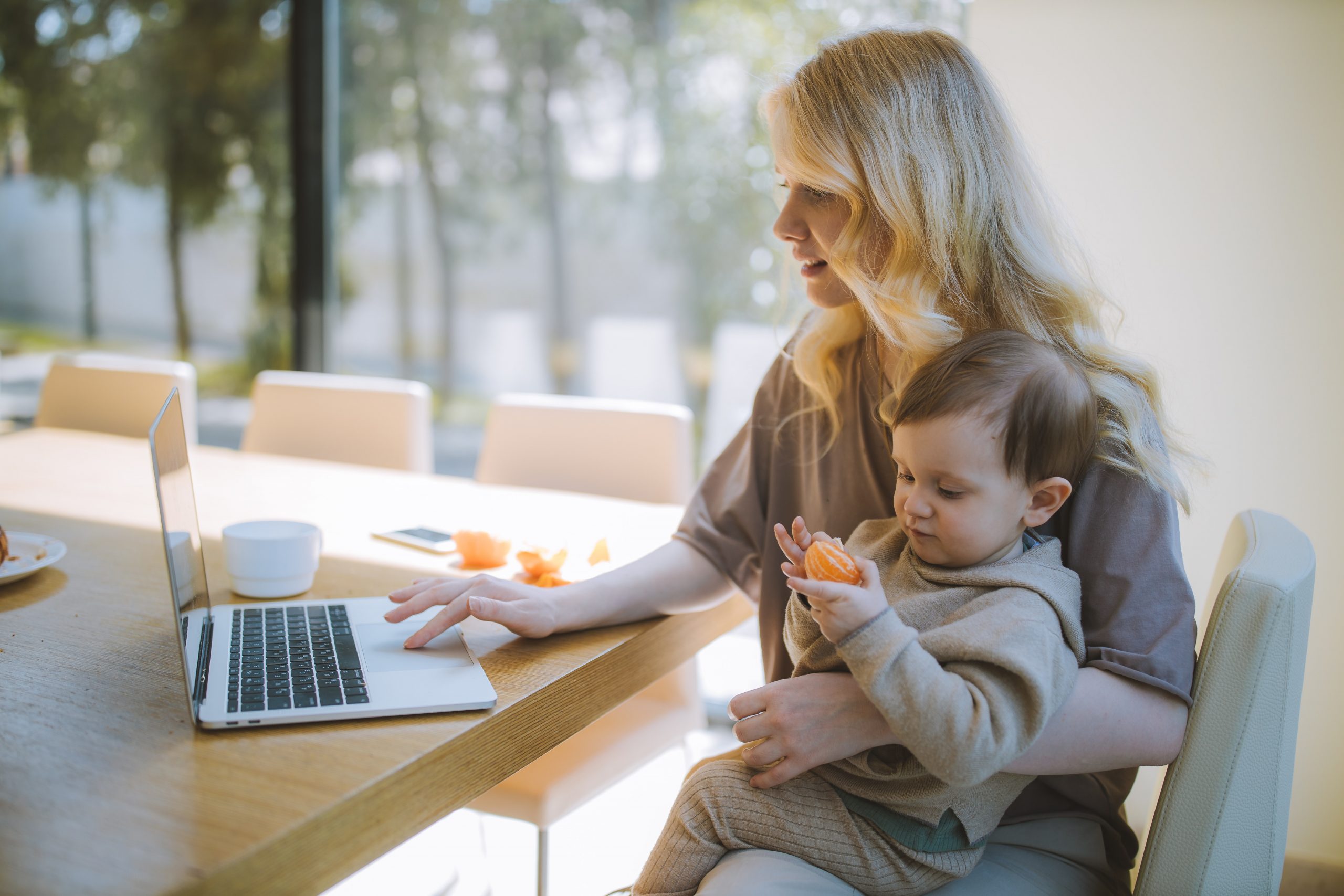 A young white woman holds her child on her lap as she works online.