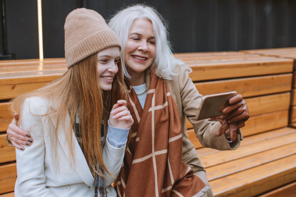 A mother and daughter take a selfie on Mother's Day while sitting on a bench outside.