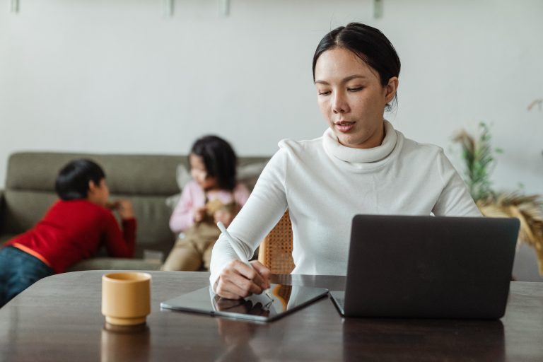 A woman works online as her kids play in the background.