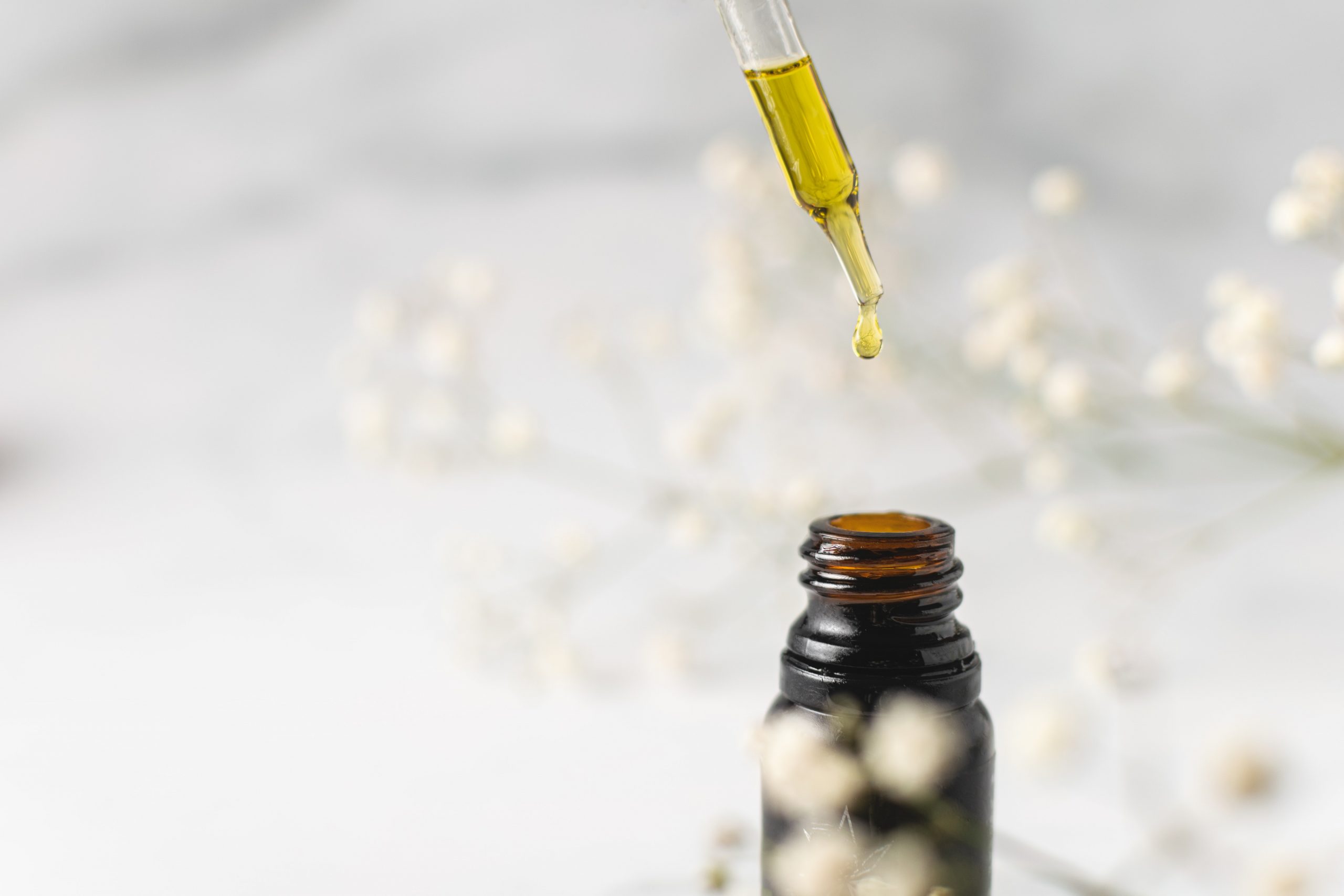 A drop of oil dripping from a pipette into a bottle of essential oil