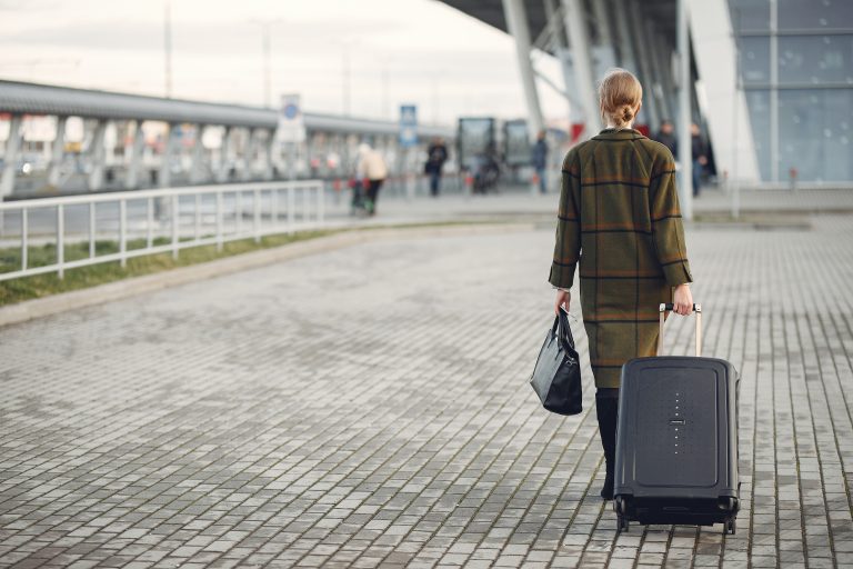A young woman with her suitcase in tow walking away.