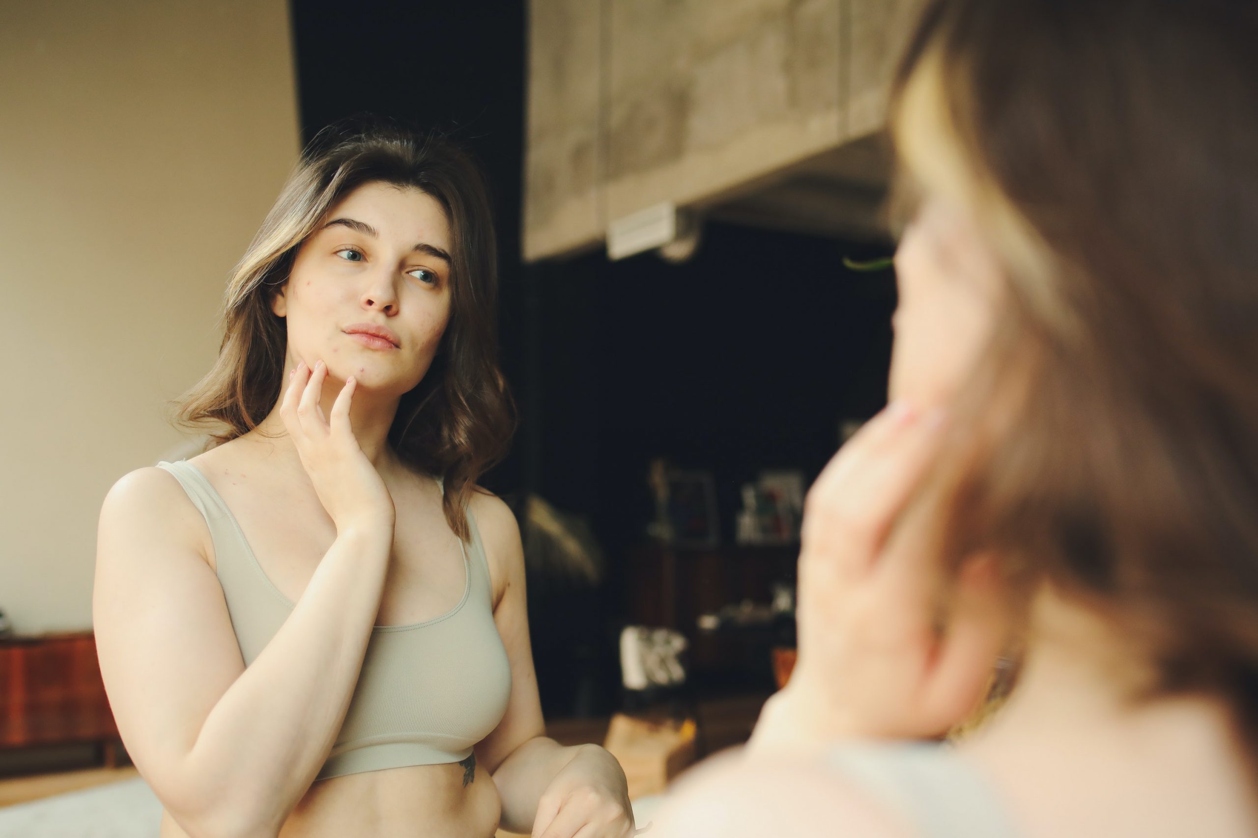A young woman examines her complexion in the mirror for hormonal acne.