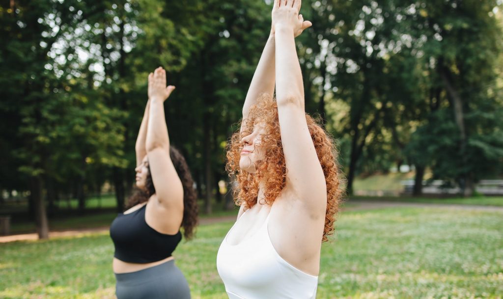 Two overweight women practise yoga in the park.