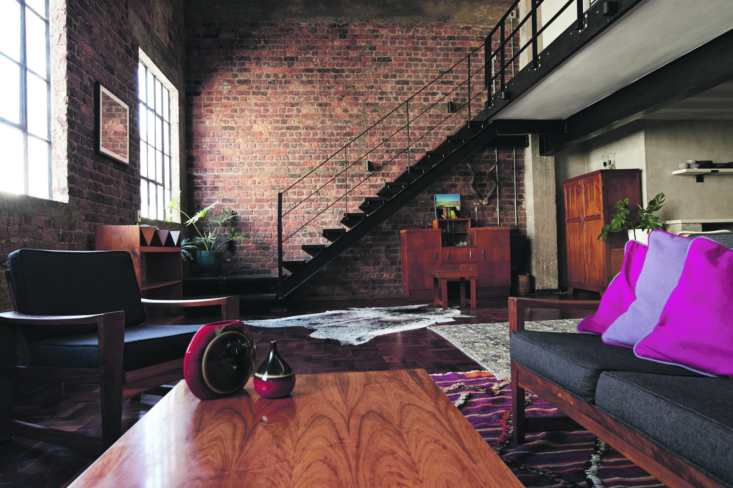 An open plan living room with a feature brick wall and a staircase running alongside it.
