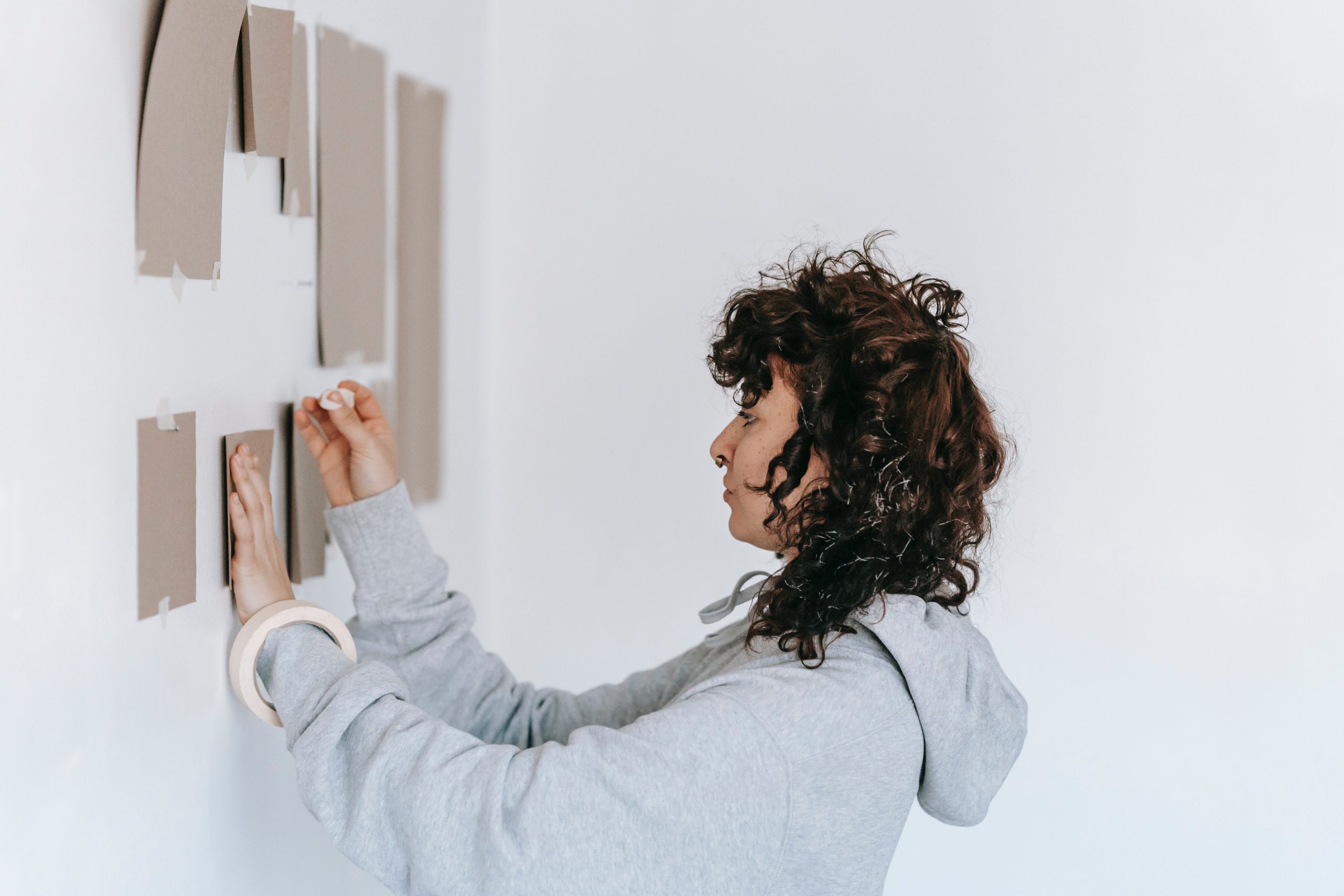 A woman trying different layouts of where to hang her pictures on the wall.
