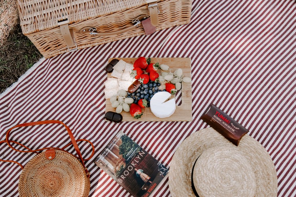 A picnic platter of cheese and fruit on a striped blanket.