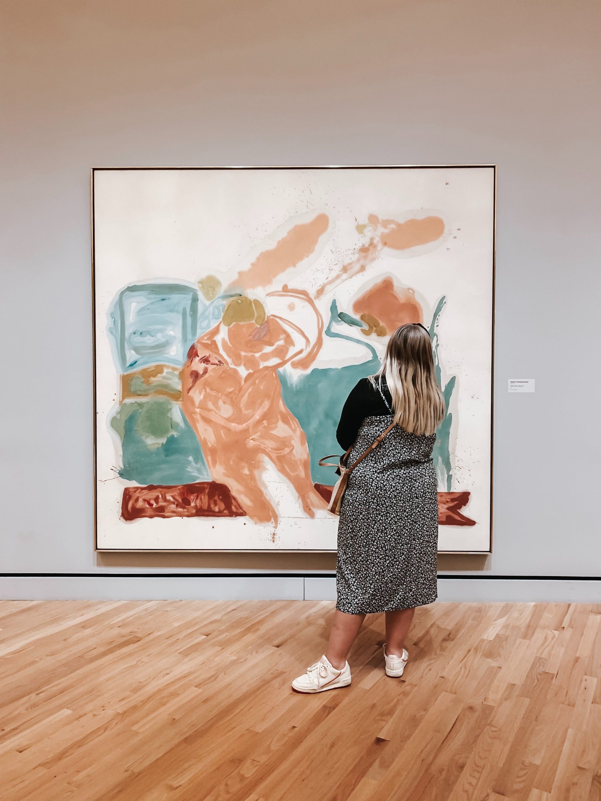 A woman in a gallery intrigued by a painting of abstract art.