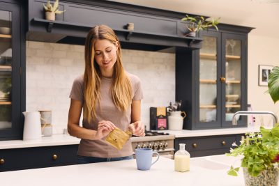 A young woman preparing a cup of Artisan Coffee in her kitchen.