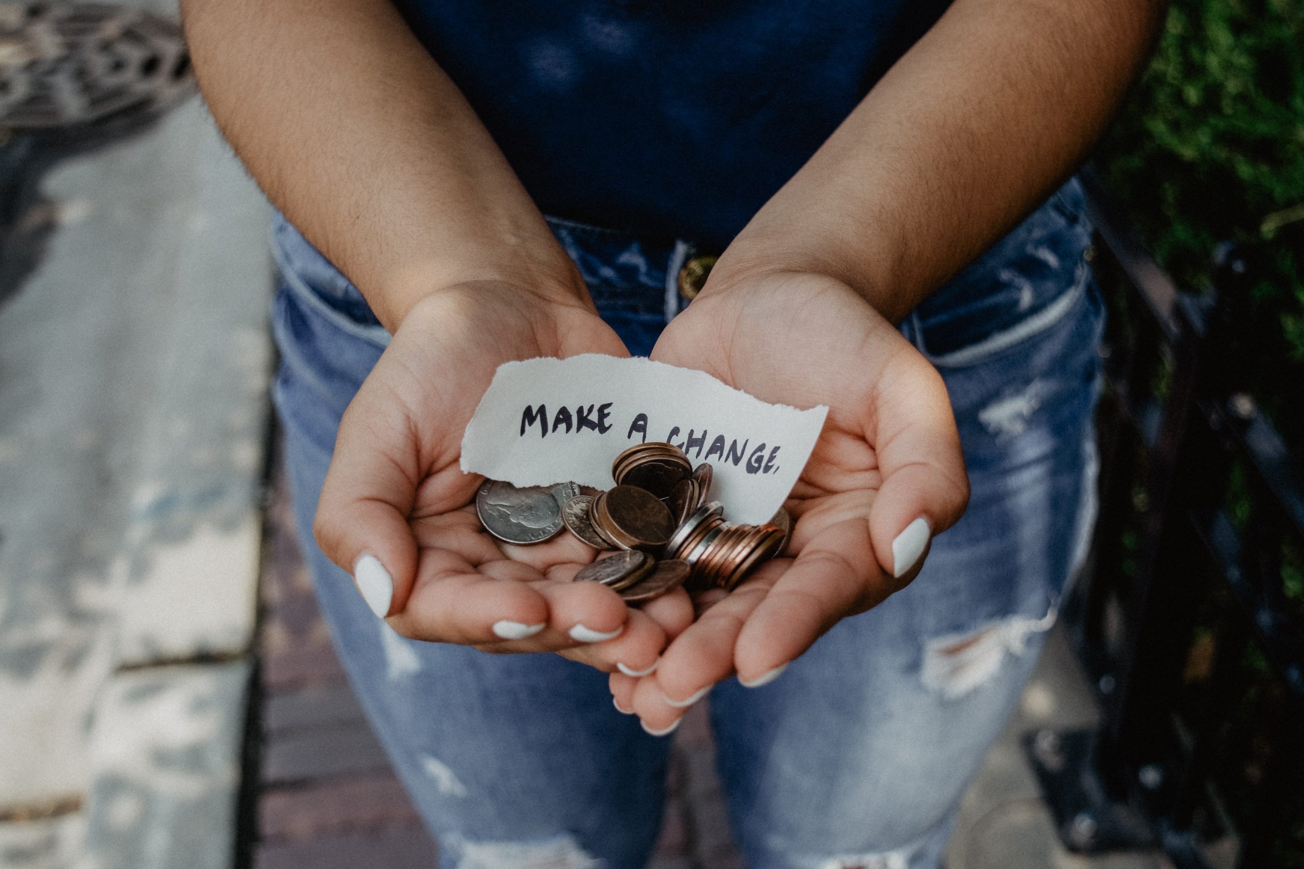 Person holding coins and a note saying 'Make a change'