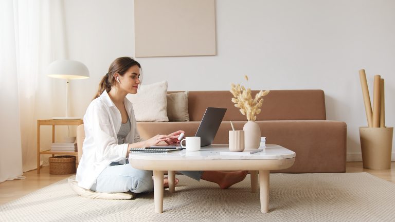 Sitting on the floor in her living room, a woman shops online on her laptop.