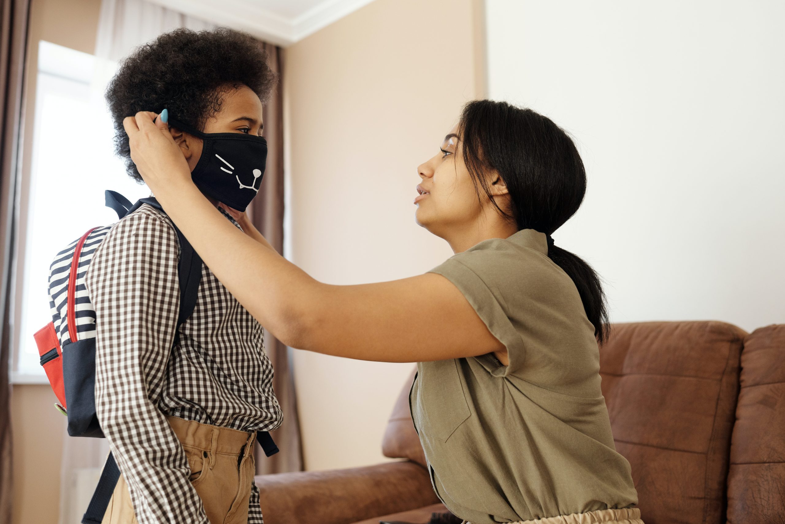 A mother adjusting her son's face mask just before he goes to school.