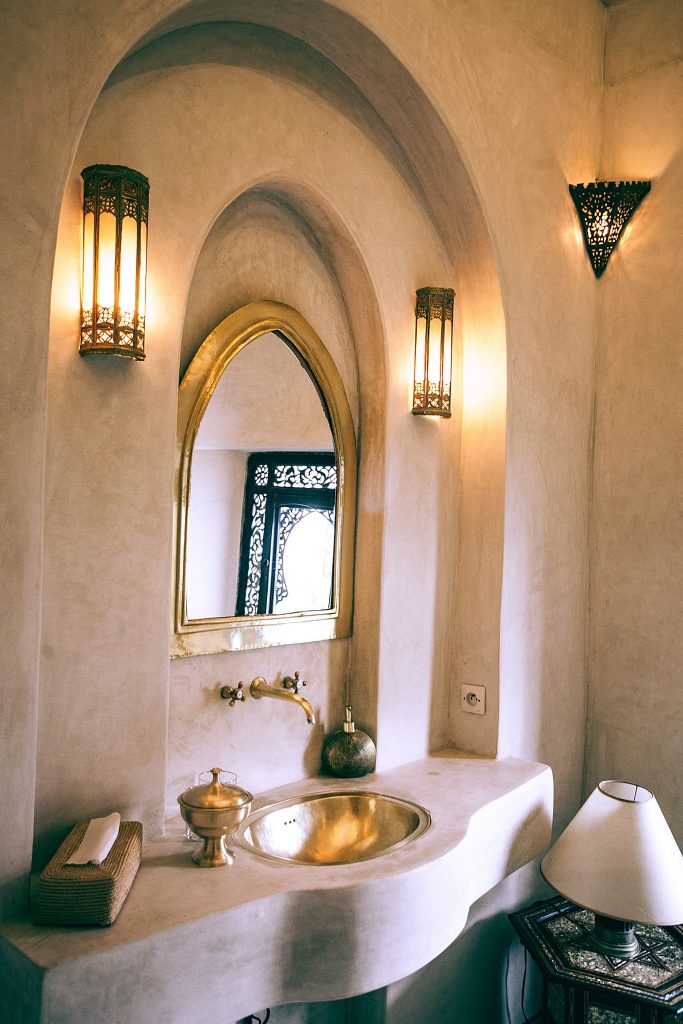 White-based, stone bathroom with golden sink, soap dispenser and mirror