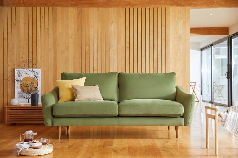Living room with olive green sofa, yellow and beige pillows, wooden wall and floor