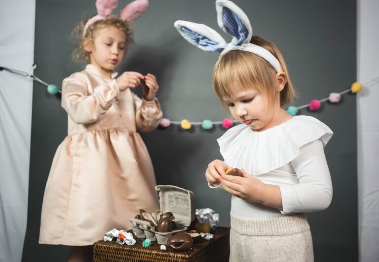Wearing Easter bunny ears headbands, two young girls enjoy their chocolate Easter eggs.