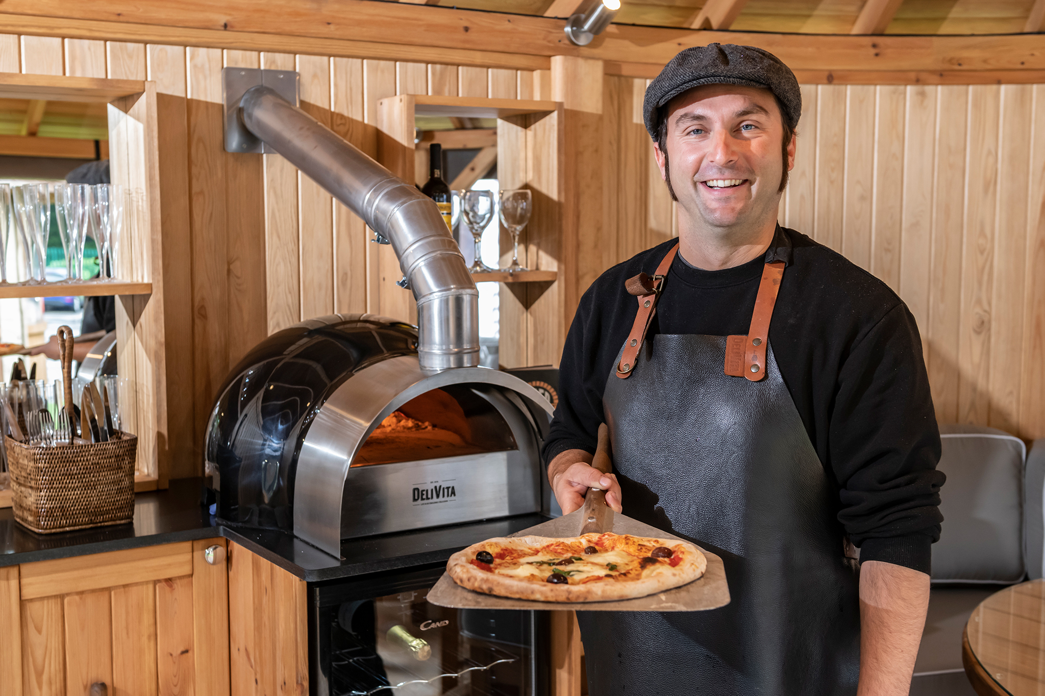 A Delivita chef presents a pizza he's just made in a Crown Pavilions garden room.