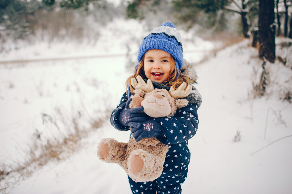 Kid in a winter forest. Girl in a blue hat. Child playing with toy